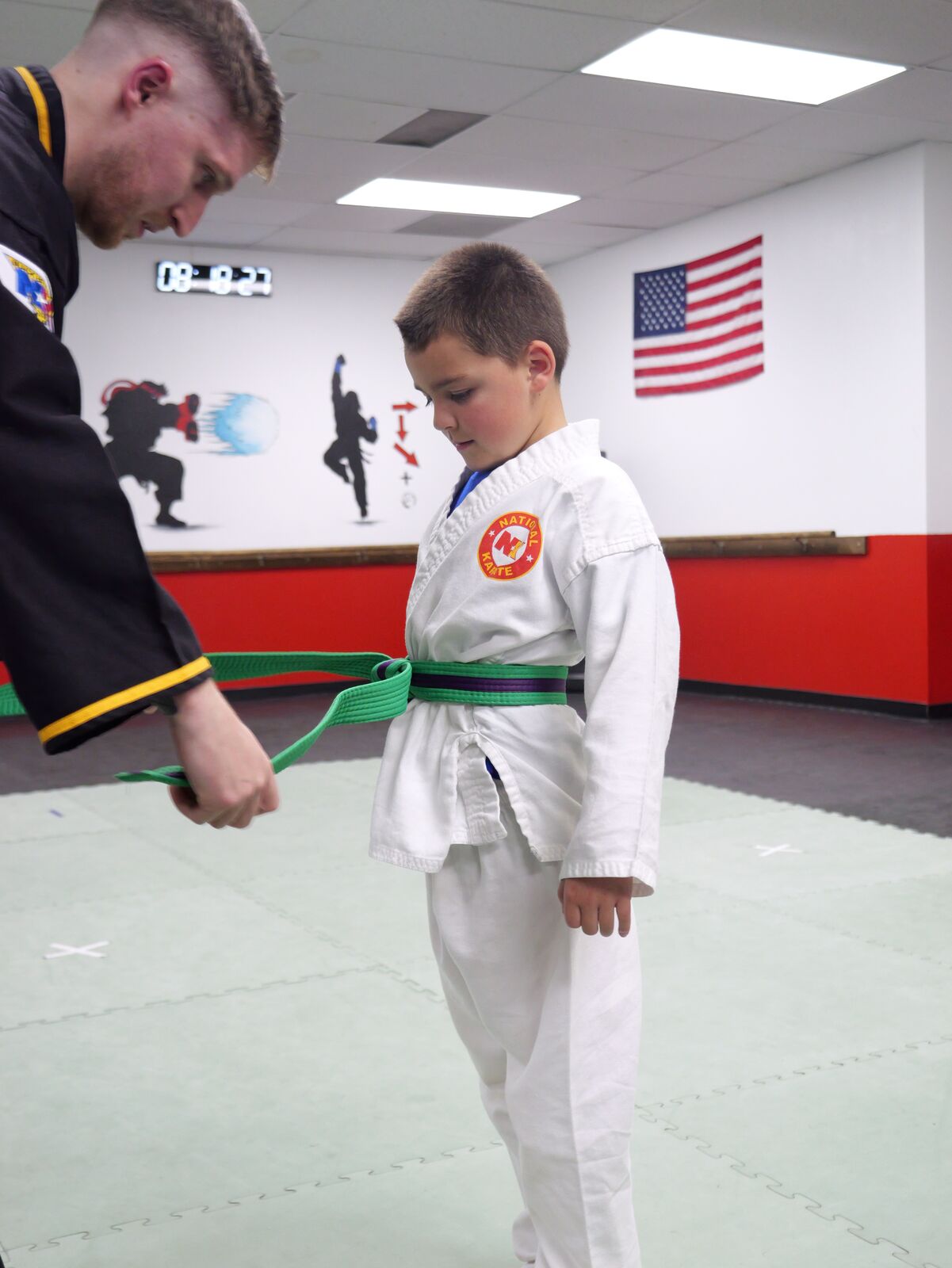 Instructor helping a young student tie a green belt